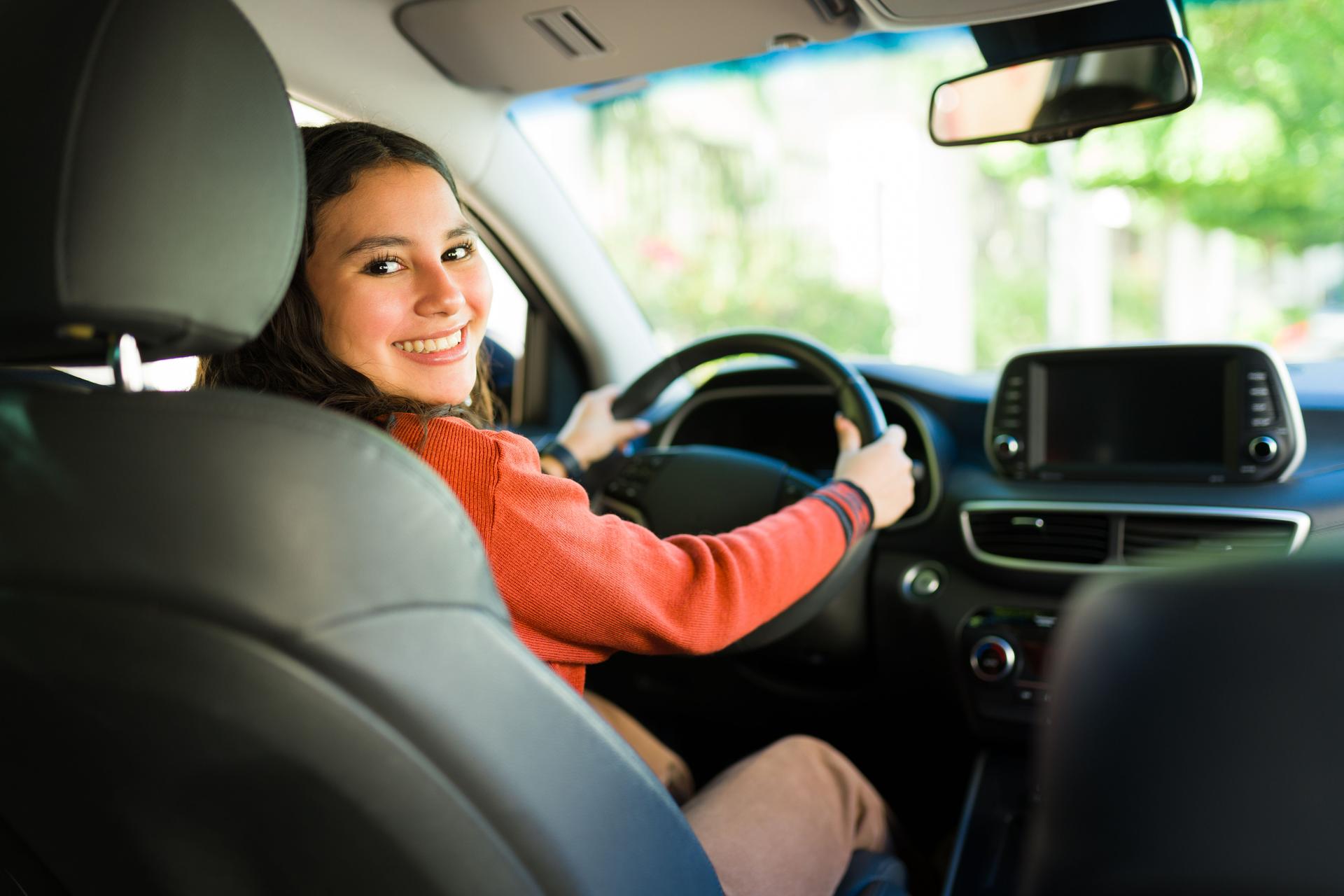 Happy teen girl smiling and enjoying driving a car from the driver's seat poses for a portrait